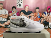 Side view of a white Nike sneaker with a dark patterned Swoosh and ankle strap detail