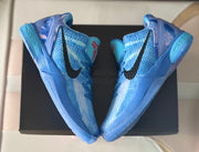 Top-down view of the pair placed over a black box, showing the blue uppers and black branding.