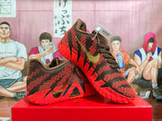 Pair of dark brown and red basketball sneakers displayed on a red shoebox, showing the textured upper, padded collar, and patterned outsole.