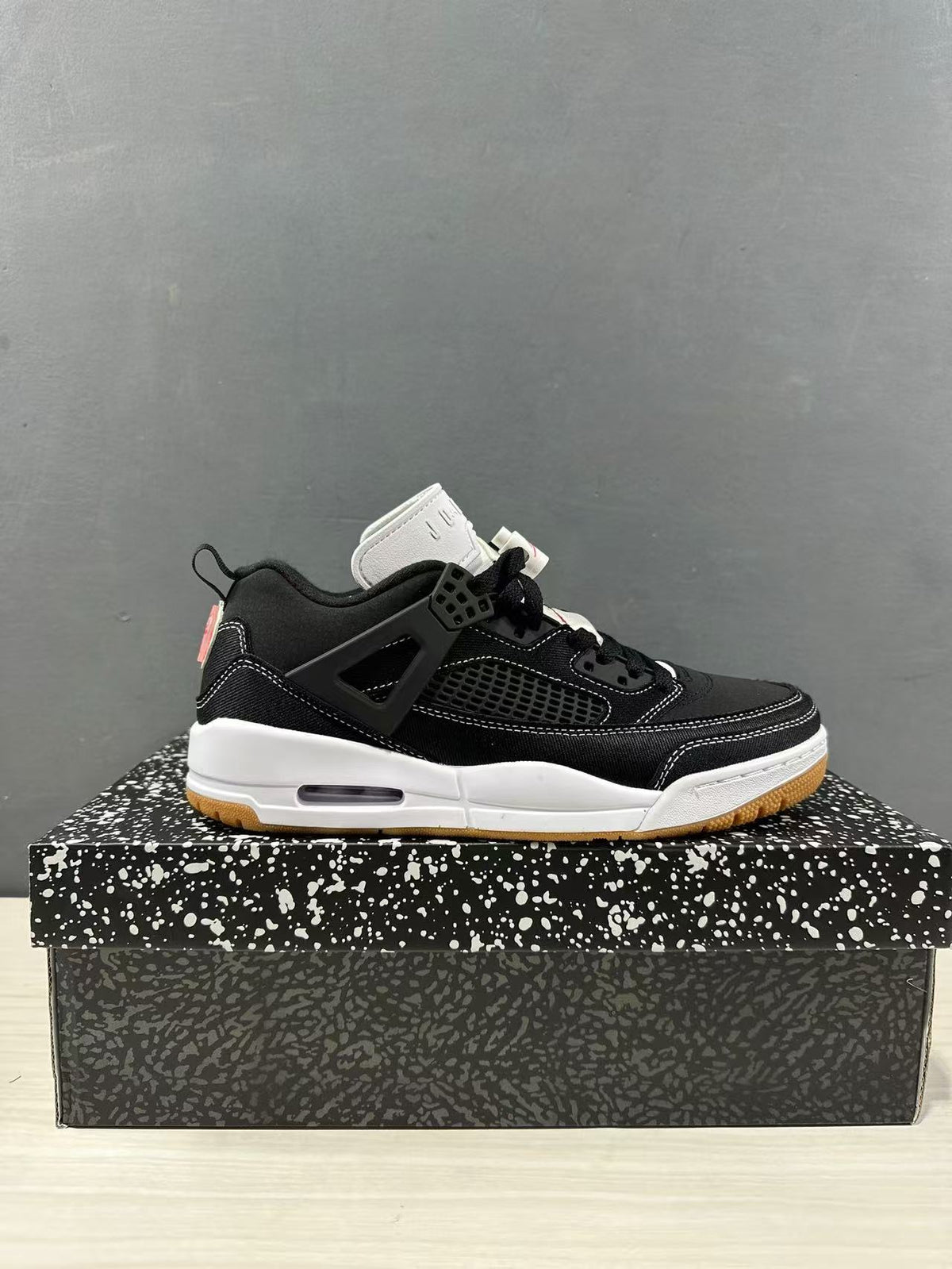 Side view of black and white Jordan Spizike Low sneakers displayed on a patterned shoe box.
