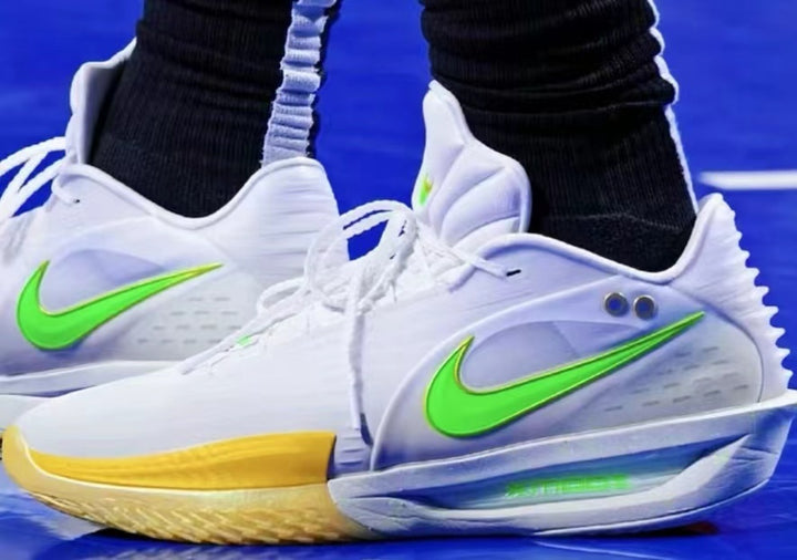 Pair of white Nike basketball-style sneakers with bright green Swoosh logos, yellow and blue-green sole accents, shown on a blue court.