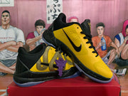 Angled view of the yellow and black sneakers showing the black Swoosh, gold side detail, purple accessory, and translucent outsoles.