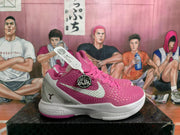 Side view of a pink and white Nike basketball sneaker showing the textured upper, white Swoosh, Kobe-related badge, and silver-gray heel panel.