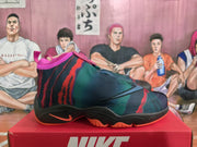 Side profile of a Nike high-top basketball sneaker showing the dark teal, red, and black upper, Nike side branding, black midsole, and orange outsole accents.