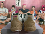 Rear view of white and tan basketball sneakers with dark green collar lining and Uncle Drew-themed artwork in the background.