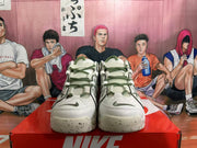 Front view of off-white Nike sneakers with dark green laces and accents, perforated uppers, and speckled soles.