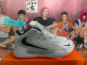 Side view of a gray and white Nike basketball shoe with dotted panels, dark Swoosh, and orange outsole.