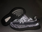 Flash-lit view highlighting the reflective detailing across the black sneaker upper.