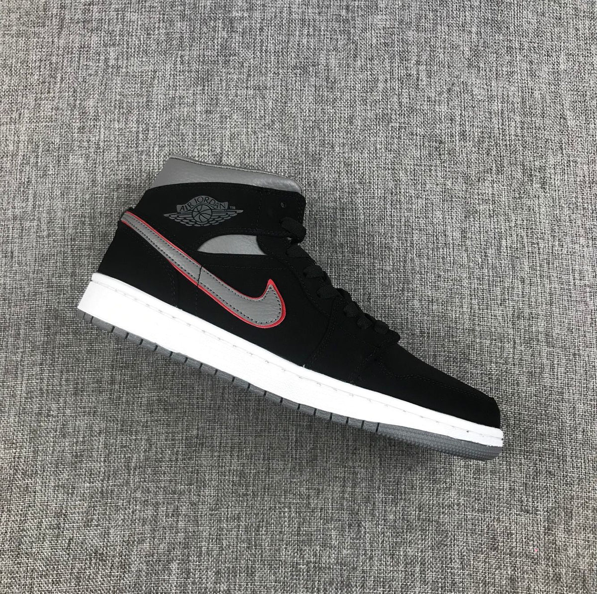 Side view of a black Air Jordan 1 Mid sneaker with a grey and red-edged Swoosh, white midsole and grey outsole.