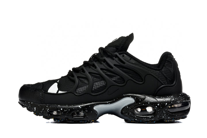 Side view of black Nike Air Max Plus sneakers with a layered mesh upper, sculpted overlay cage, visible cushioning, and a speckled midsole.
