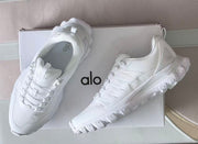 Angled top and side views of white Alo sneakers on a box.