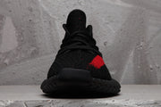 Front view of the black lace-up sneaker with a black toe, red side detail, and textured sole.