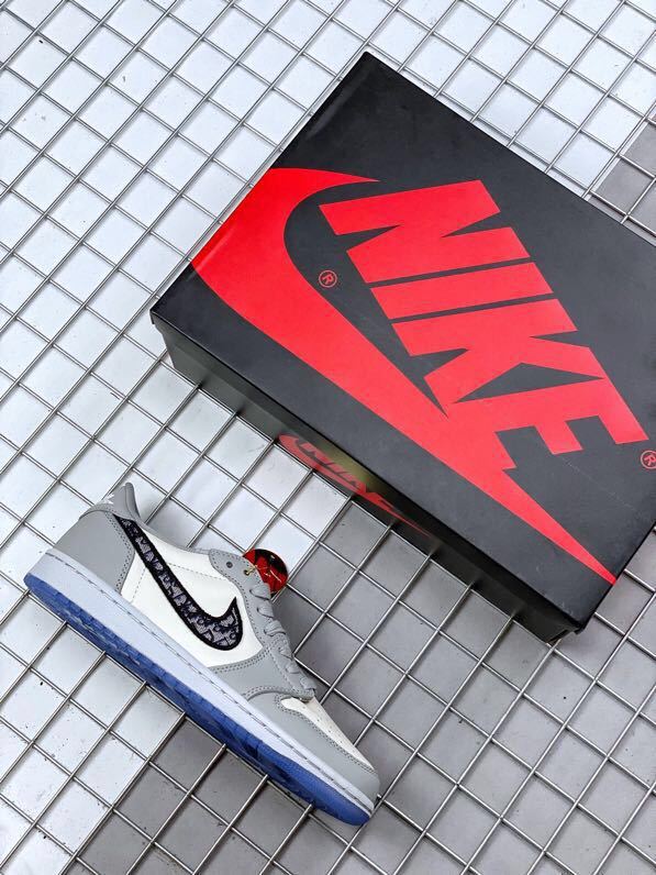 Grey and white low-top sneaker beside a black and red Jordan shoebox, showing a patterned black Swoosh and translucent blue outsole.