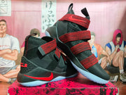 Angled view of the black and red strapped Nike LeBron basketball shoes.