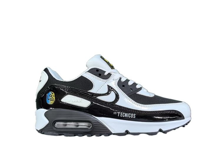 Side view of black, white, and gray Nike Air Max 90 sneakers with a visible heel cushioning unit and “Los Técnicos” side text.