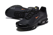 Angled view of black Nike Air Max Plus VII sneakers with orange accents and perforated uppers
