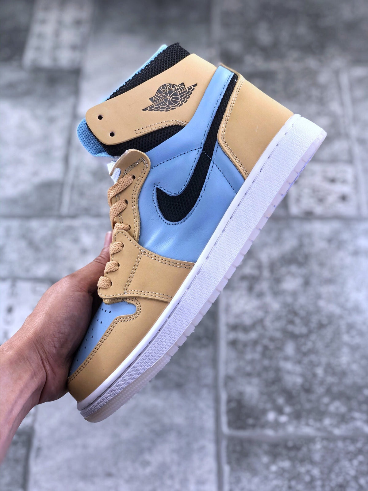 Close-up side view of a tan and light blue Jordan high-top sneaker with black Swoosh, winged emblem, and white outsole.