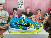 Side view of blue and yellow Nike basketball sneakers with a graphic patterned upper, black Swoosh, white midsole, and yellow outsole.