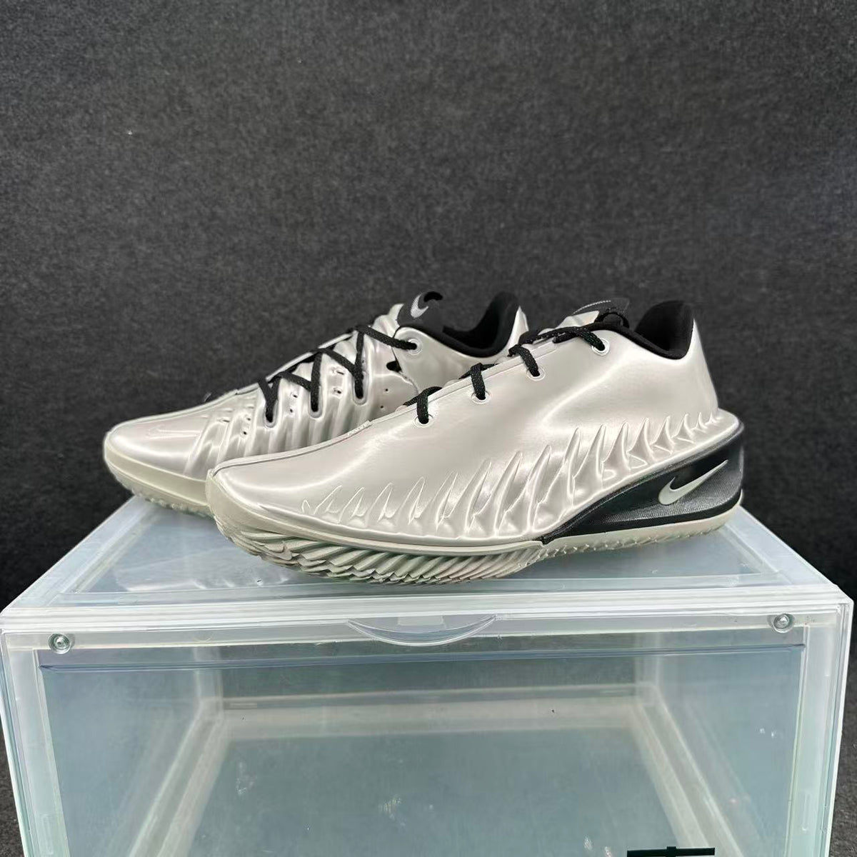 Pair of metallic silver Nike sneakers with black laces and black midsole accents shown from a front three-quarter angle.