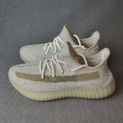 Pair of silver-toned 350 V2 sneakers shown from the side with olive stripes and ribbed translucent soles.