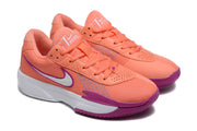 Angled view of the coral Nike sneaker pair with purple accents, laces, perforated overlays, and white midsoles.