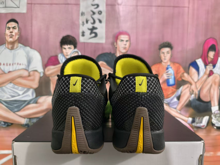 Rear view of black Nike basketball sneakers showing yellow details, gray patterned panels, and brown-and-yellow outsole accents.