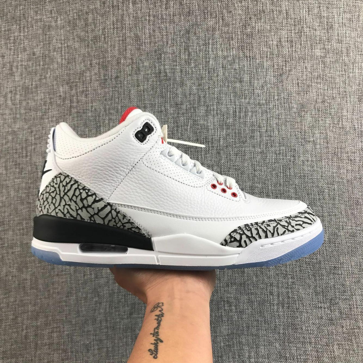 Side view of a white Jordan Air Jordan 3 sneaker with grey-and-black elephant-print overlays, red accents, and a translucent blue outsole.