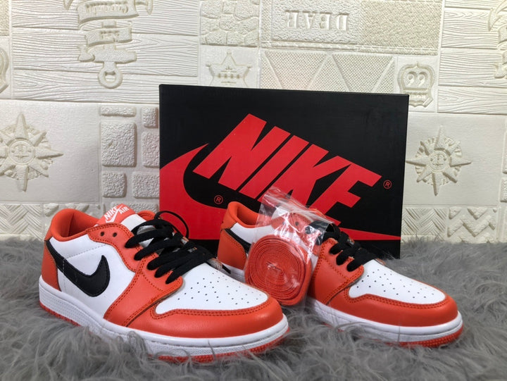 Pair of white, orange and black low-top sneakers displayed with a black Nike shoebox and an extra orange lace set.