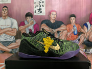 Side view showing the green patterned upper, gold Swoosh, yellow lace charm, and purple outsole.