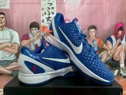 Angled view of the blue and white Nike basketball sneakers showing both sides, textured uppers, white Swoosh branding, blue outsoles, and red accents.