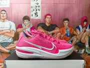 Side profile of a pink and white Nike basketball sneaker showing the mesh upper, white Swoosh, and structured sole.
