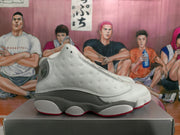 Side profile of a white and gray high-top Jordan sneaker showing perforated side panels, layered construction, and a red outsole edge.