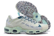 Side view of a white and teal Nike Air Max Tn sneaker with its speckled outsole visible.