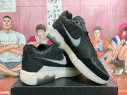 Angled view of a pair of black Nike sneakers showing gray swooshes, tonal heel graphics, and light-colored soles.