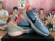 Angled view showing the textured blue upper, black Swoosh, white laces, coral accents, and speckled midsole.