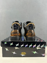 Rear view of black Jordan Air Jordan 6 sneakers with bronze-toned heel detailing on a patterned shoebox.