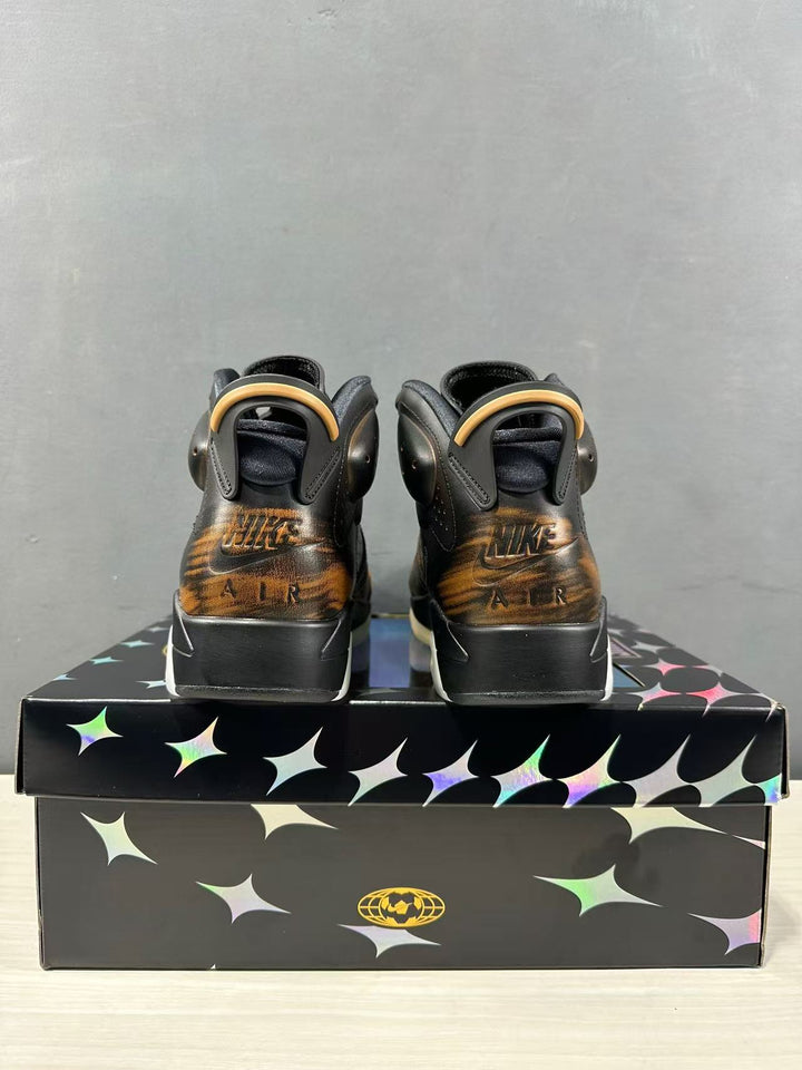 Rear view of black Jordan Air Jordan 6 sneakers with bronze-toned heel detailing on a patterned shoebox.
