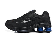 Side view of a black Nike Shox R4 sneaker with silver Swoosh details and blue cushioning columns.
