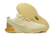 Pale yellow Nike basketball shoes with gold-toned heel accents.