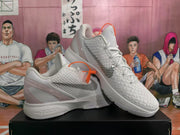 Angled view of paired white and silver Nike basketball sneakers highlighting the textured upper, side detailing, padded collar, and orange lace accessories.