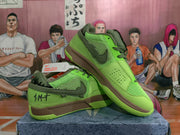 Angled product view showing the green Nike sneakers, dark Swoosh branding, mesh upper, and contrasting brown midsole.
