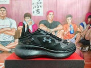 Side profile of a black Under Armour basketball sneaker with gray panel details and a textured sole.