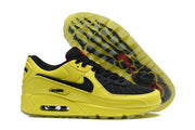 Side and outsole views of yellow and black Nike Air Max 90 sneakers.