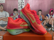Angled view showing the red upper, yellow side detailing, green accents, laces, and ZoomX branding.