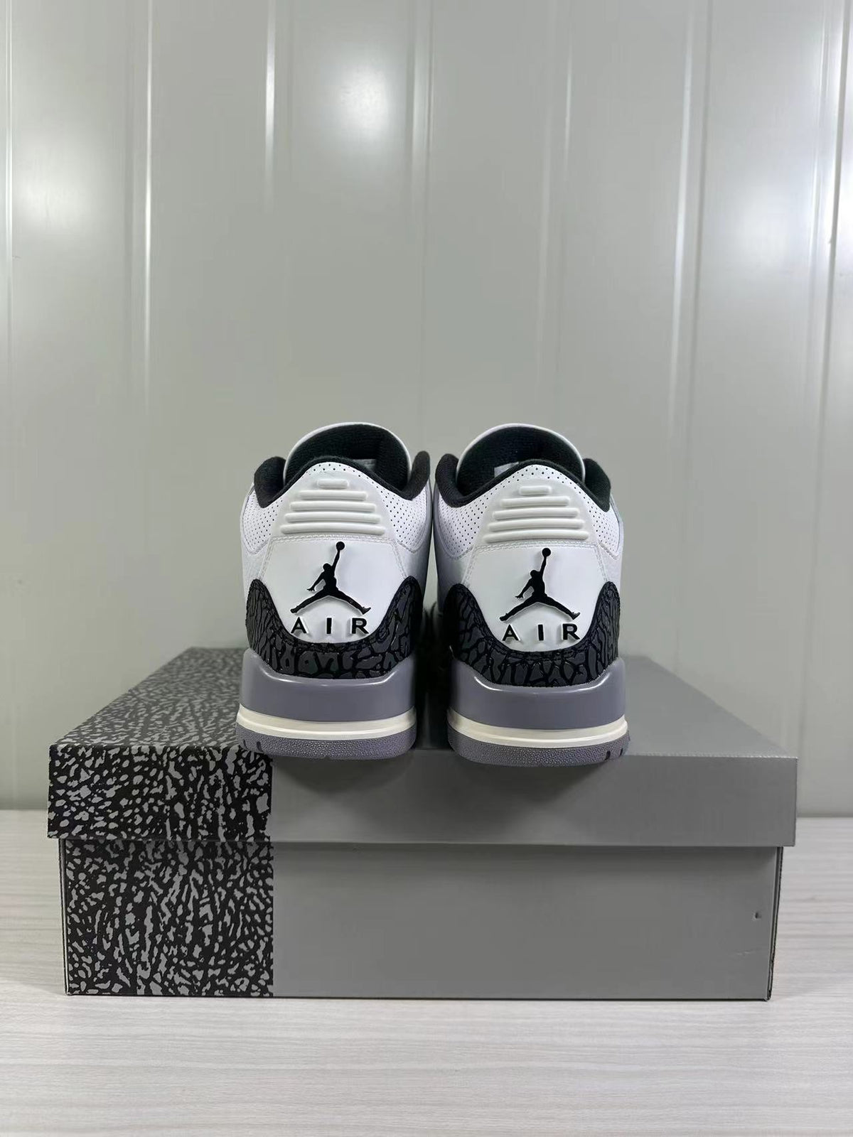 Rear view of white and grey Air Jordan 3 sneakers displayed on a patterned shoebox.