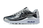 Side profile of a silver and black Nike Air Max 90 sneaker with white midsole and visible cushioning window.
