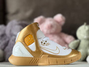 Side profile of gold and white Nike Kobe 2K5 kids' basketball shoes with a high ankle collar and patterned outsole.