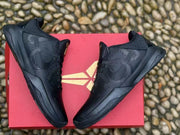 Overhead view of both black sneakers on a red box, showing the side detailing and black midsoles.