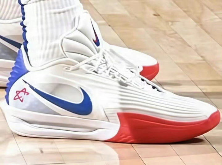Pair of white high-top Nike basketball sneakers with blue Swoosh logos and red outsole accents on a court floor.