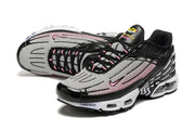 Angled view of the black, white, and pink Nike Air Max Plus sneakers showing the mesh-patterned upper and pink accents.